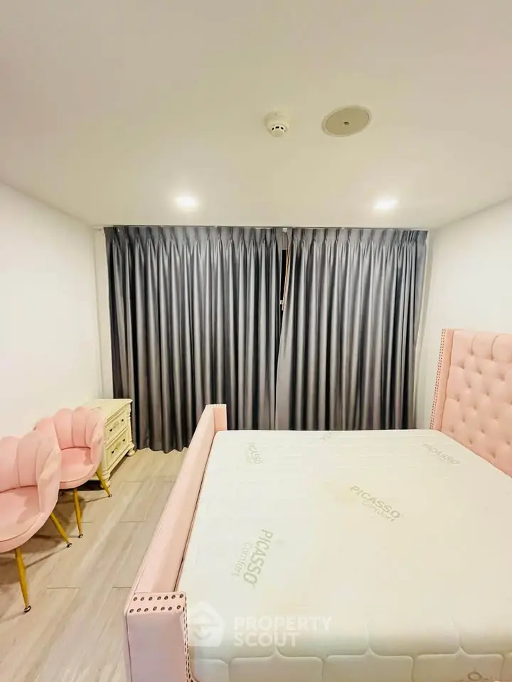 Spacious bedroom with elegant pink bed and stylish chairs, featuring modern lighting and floor-to-ceiling curtains.