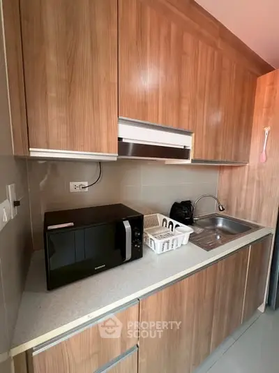 Modern kitchen with wooden cabinets and sleek countertop featuring a microwave and sink.