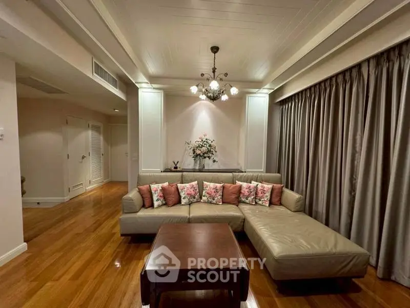 Elegant living room with plush sectional sofa and floral accents, featuring warm wooden flooring and ambient lighting.