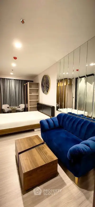 Modern bedroom with blue sofa and mirrored wall, featuring stylish decor and cozy ambiance.