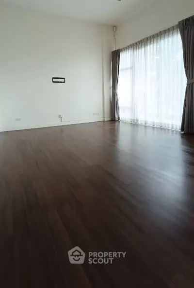 Spacious empty living room with elegant wooden flooring and large windows.