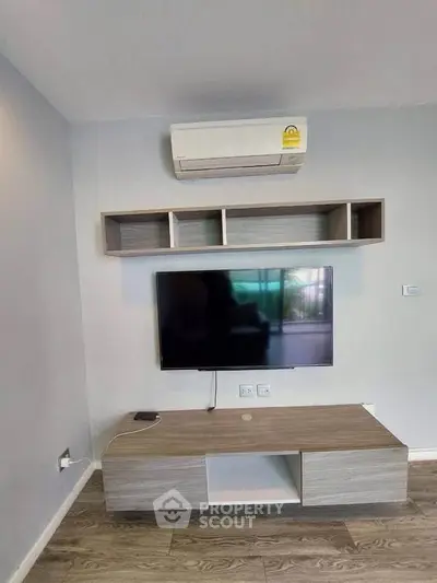 Modern living room with wall-mounted TV and air conditioning unit, featuring sleek wooden furniture.