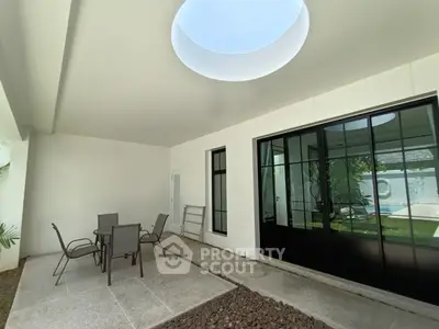 Modern patio with skylight and outdoor seating, adjacent to a pool area.