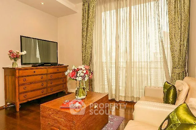 Charming living room with elegant decor, featuring a TV, wooden furniture, and large window with sheer curtains.