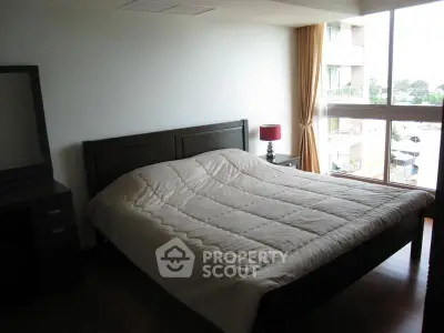 Spacious bedroom with large window and modern furniture in a stylish apartment.