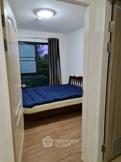 Cozy bedroom with wooden flooring and large window offering natural light.