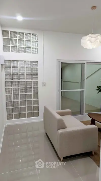 Modern living room with sleek design and glass block wall, featuring a cozy beige sofa and stylish lighting.
