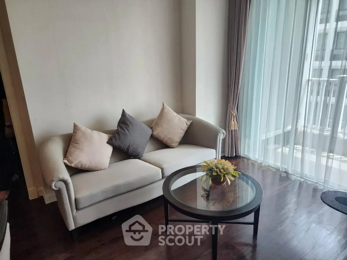 Cozy living room with elegant sofa and glass coffee table near large window with sheer curtains.
