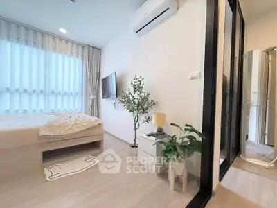 Modern bedroom with stylish decor, featuring a cozy bed, air conditioning, and natural light through large windows.