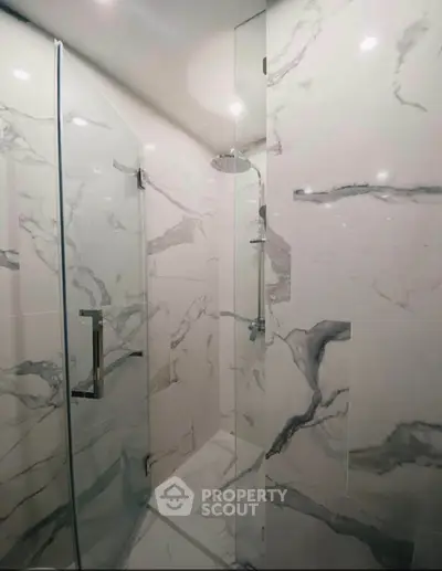 Luxurious marble-tiled shower with sleek glass door in modern bathroom.