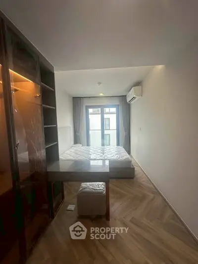 Modern bedroom with large window and wooden flooring in a stylish apartment.