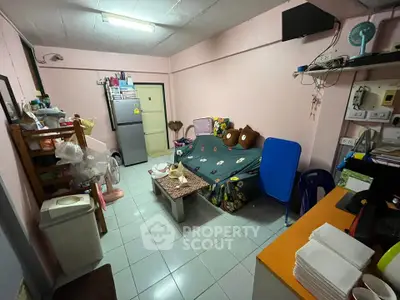 Cozy living room with sofa, fridge, and organized shelves in compact apartment.