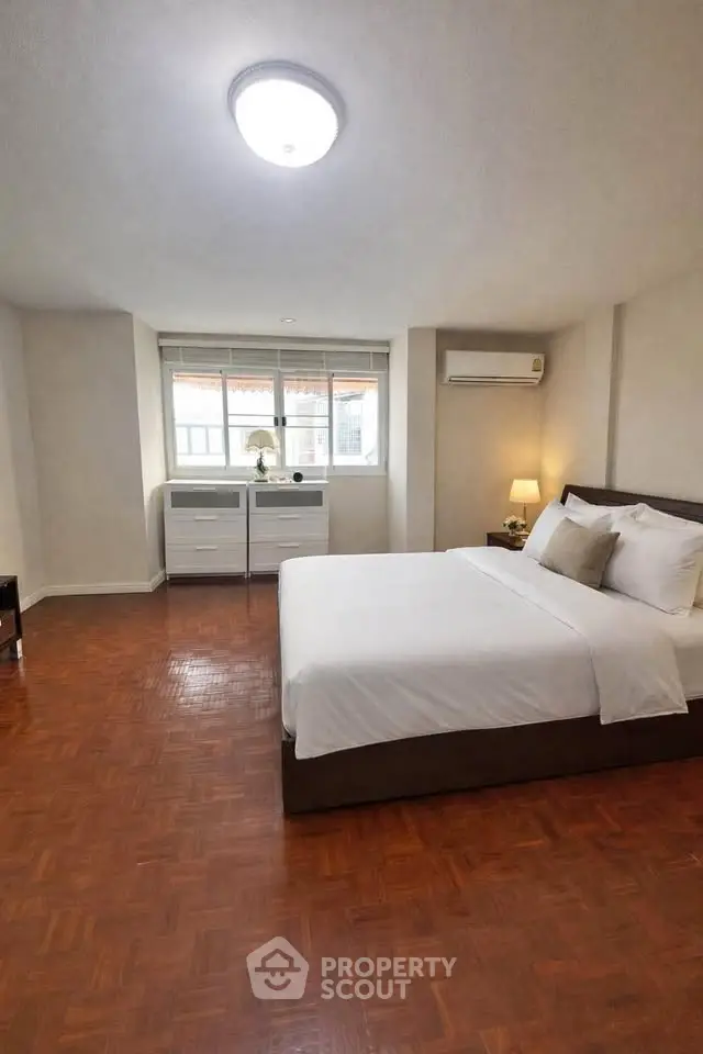 Spacious bedroom with wooden flooring and large window offering natural light.