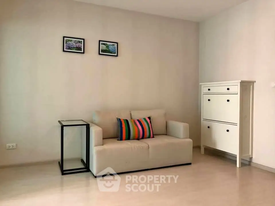 Modern minimalist living room with beige sofa and colorful pillow, perfect for cozy relaxation.