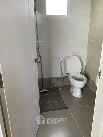 Compact bathroom with modern fixtures and neutral tiles, featuring a toilet and shower area.
