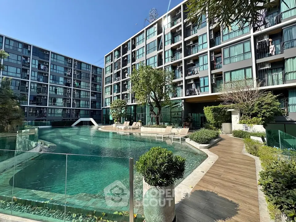 Modern apartment complex with large swimming pool and sun loungers, perfect for relaxation and leisure.