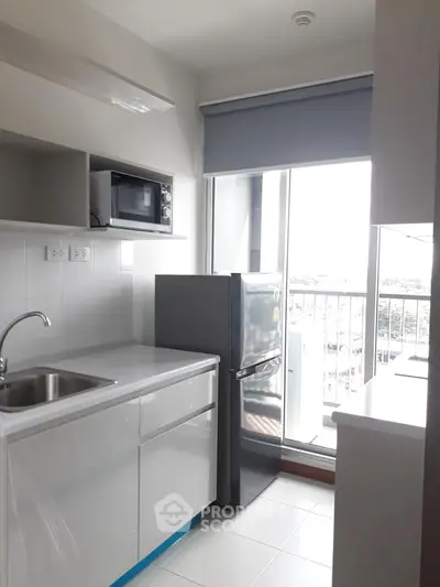 Modern kitchen with sleek cabinetry, stainless steel fridge, and microwave, featuring a balcony view.