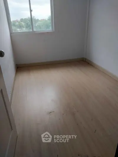 Spacious empty bedroom with wooden flooring and large window offering natural light.