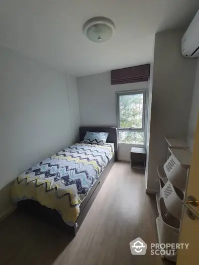 Cozy bedroom with ample natural light, modern air conditioning unit, and a serene view of greenery outside the window, perfect for restful living.