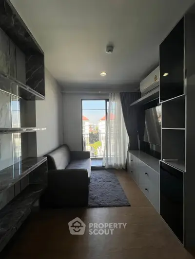 Modern living room with sleek furniture and large window offering natural light and city view.