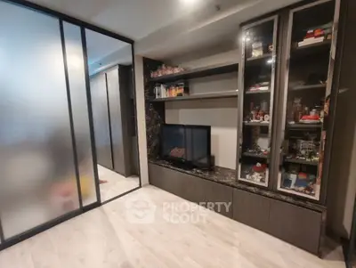Modern living room with sleek storage and TV unit, frosted glass partition, and wooden flooring.
