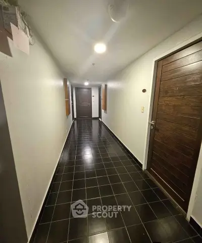 Spacious apartment corridor with sleek black tile flooring and wooden doors.