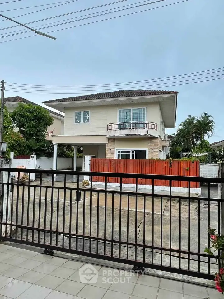 Charming two-story house with balcony and gated entrance in a serene neighborhood.