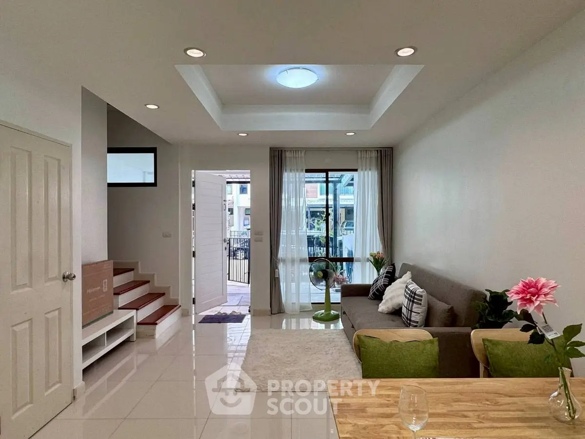 Modern living room with stylish decor and natural light, featuring a cozy sofa and elegant ceiling design.