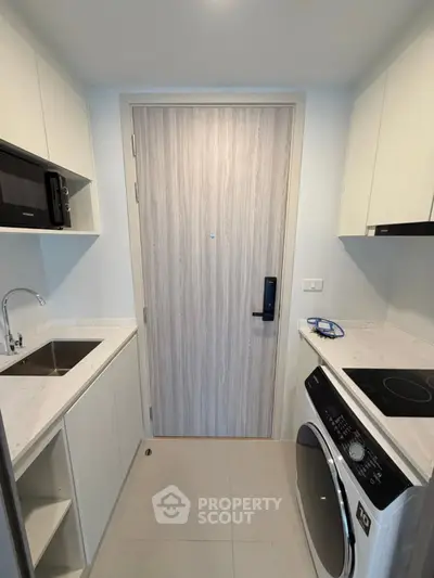 Modern compact kitchen with sleek appliances and washer-dryer combo in a stylish apartment.