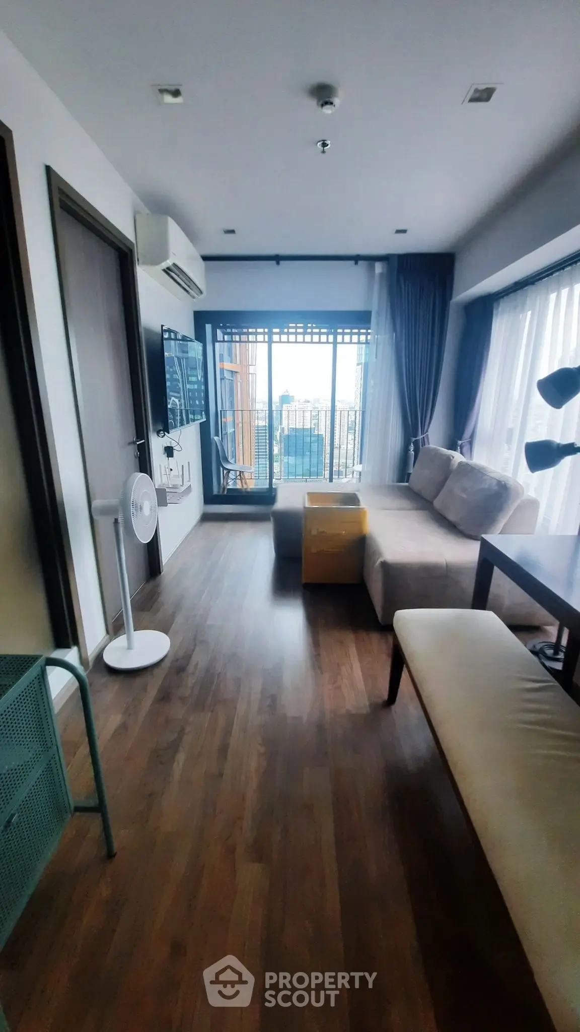 Modern living room with large windows and city view, featuring stylish furniture and wooden flooring.