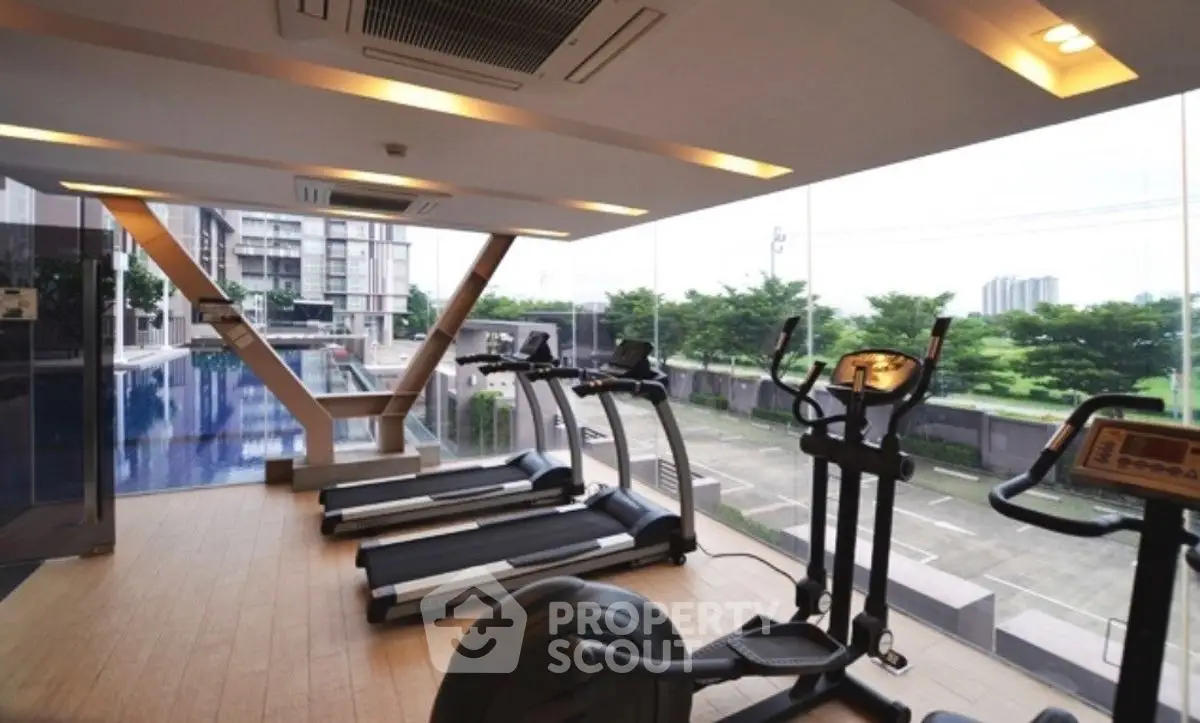 Modern gym with treadmills and exercise equipment overlooking a pool and cityscape.