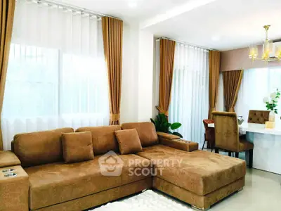 Elegant living room with plush brown sofa and dining area, featuring large windows and stylish curtains.