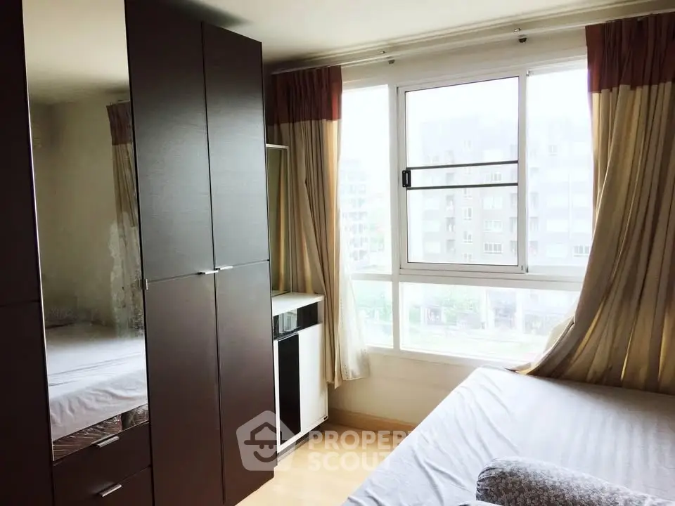 Bright bedroom with large window and modern wardrobe in urban apartment.