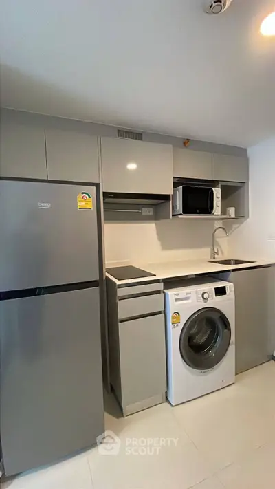 Modern kitchen with sleek appliances including fridge, washing machine, and microwave in compact layout.