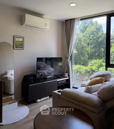 Cozy living room with large window and lush greenery view, featuring modern furniture and air conditioning.