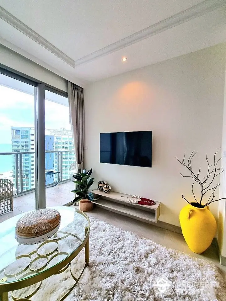 Modern living room with balcony view, stylish decor, and large TV in luxury apartment.