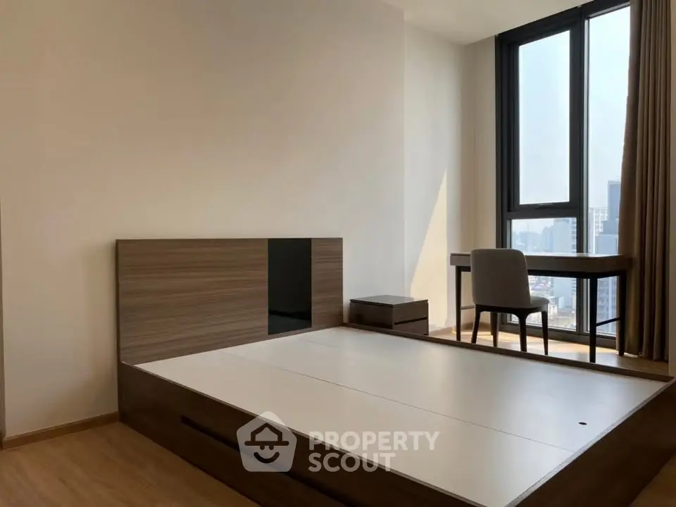 Modern bedroom with large window and study desk, offering city views and natural light.