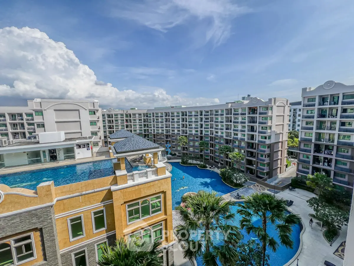 Luxurious condominium complex with stunning pool and lush landscaping under a clear blue sky.