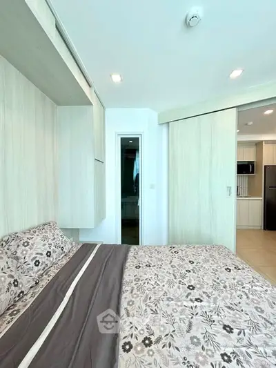 Modern bedroom with floral bedding and sliding door to kitchen area.