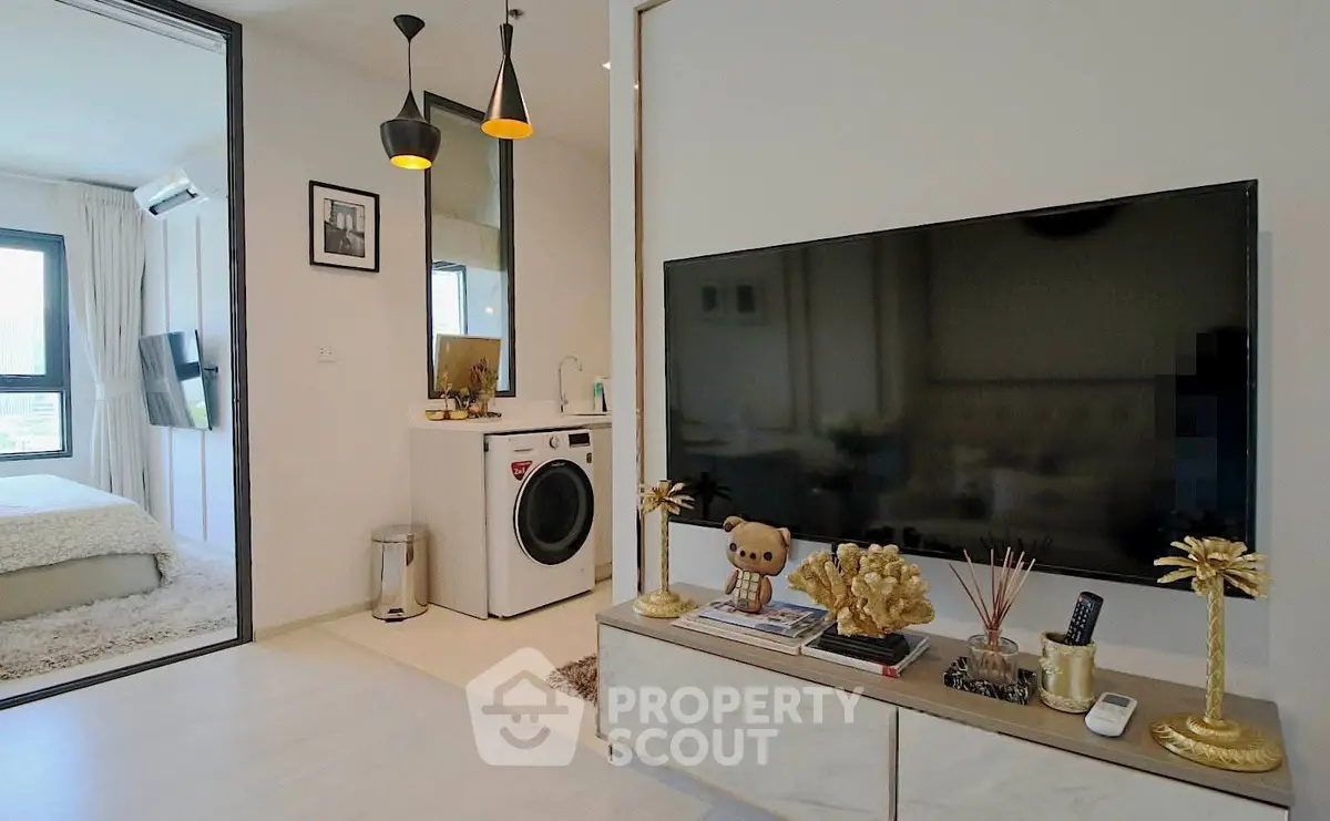 Modern living room with stylish decor and in-unit washing machine, adjacent to a cozy bedroom.