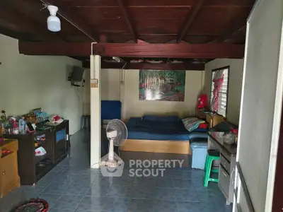 Cozy living room with wooden ceiling and tiled floor, featuring a bed, fan, and TV for a comfortable living space.