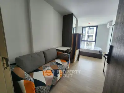 Modern studio apartment with stylish sofa and bed, featuring large window for natural light.