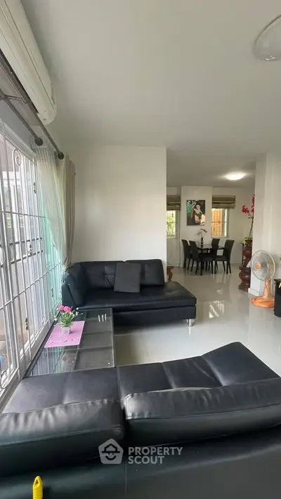 Modern living room with sleek black leather sofas and dining area in open layout.
