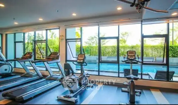 Modern gym with large windows overlooking a pool, featuring state-of-the-art exercise equipment.