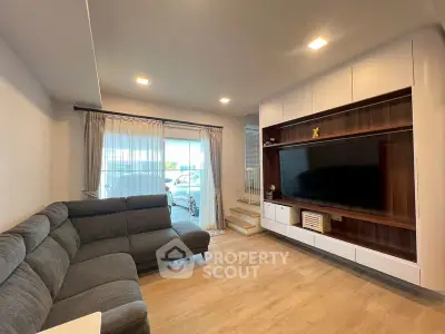 Modern living room with sleek furniture and large TV, featuring a cozy sectional sofa and stylish wooden flooring.