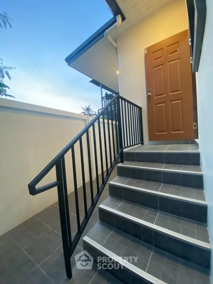 Modern exterior staircase with sleek black railing leading to a wooden door, perfect for stylish home entry.