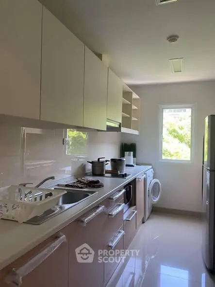Modern kitchen with sleek cabinets and appliances, featuring a washing machine and bright natural light.