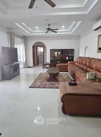 Spacious living room with leather sectional, TV, and elegant ceiling design.