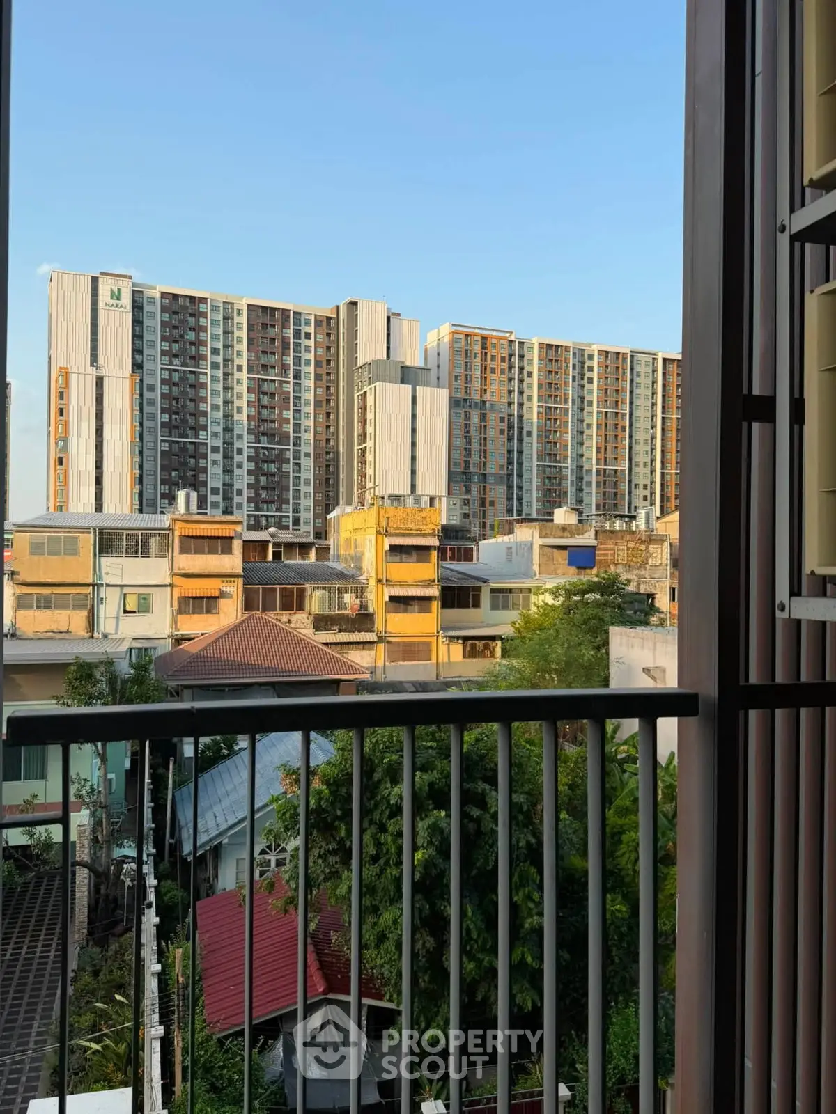 Stunning cityscape view from a balcony overlooking modern high-rise buildings and lush greenery.