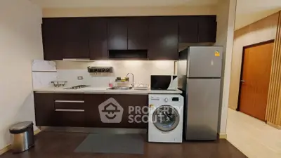 Modern kitchen with dark cabinets, washing machine, and stainless steel fridge in a cozy apartment.
